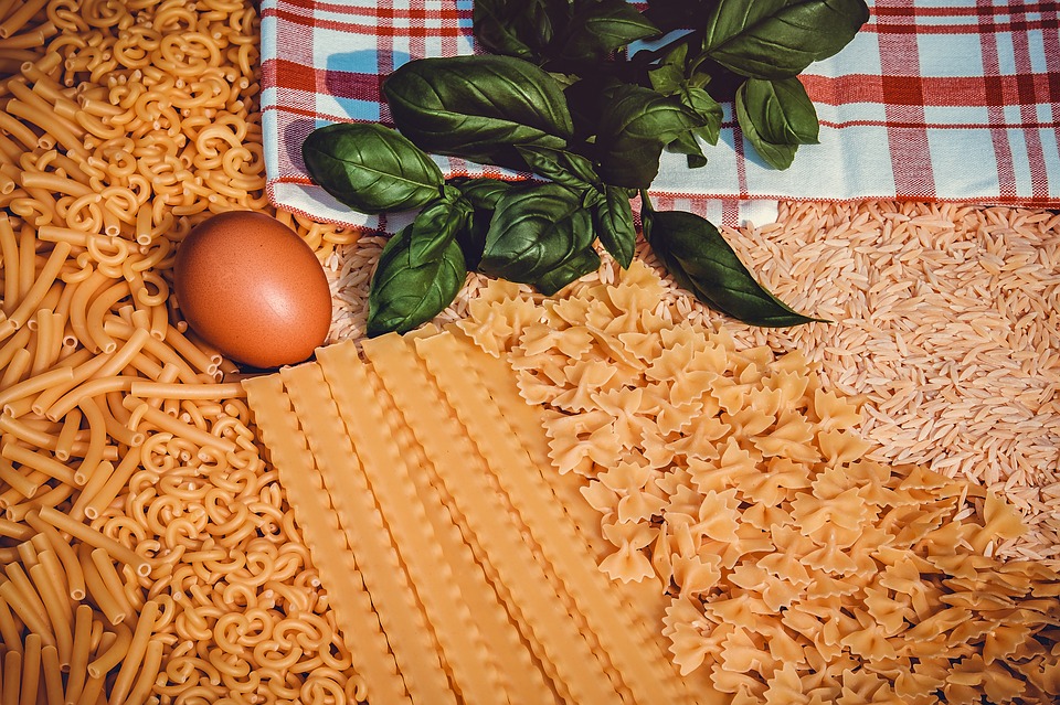 A picture of different shapes and types of dried pasta, garnished with a tomato and spinach leaf