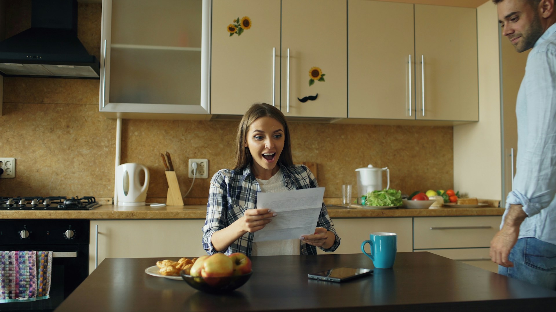 Family paperwork and a laptop spread across a kitchen table with moving boxes behind